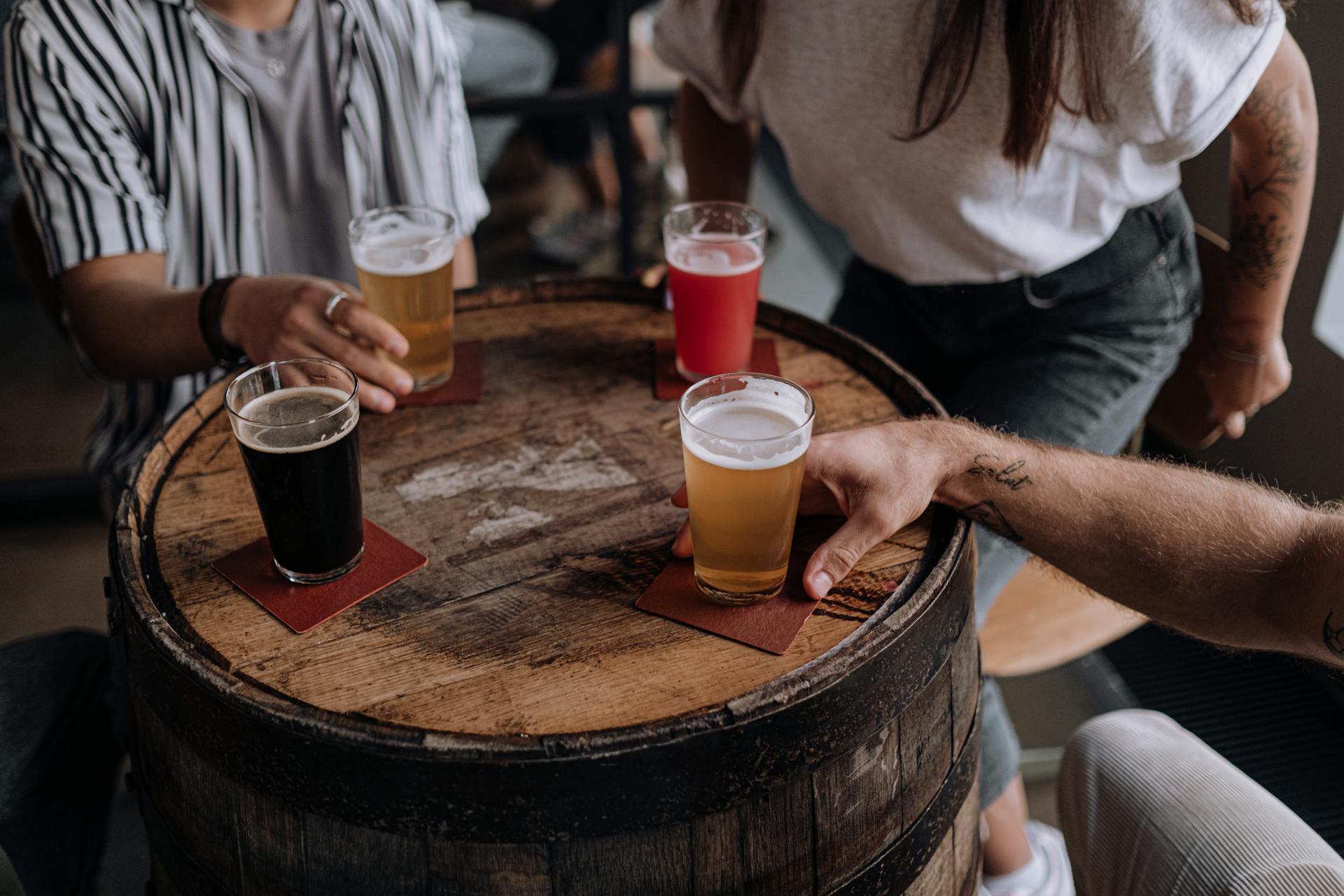 Group of people sitting around a beer barrel with a variety of filled beer glasses on top